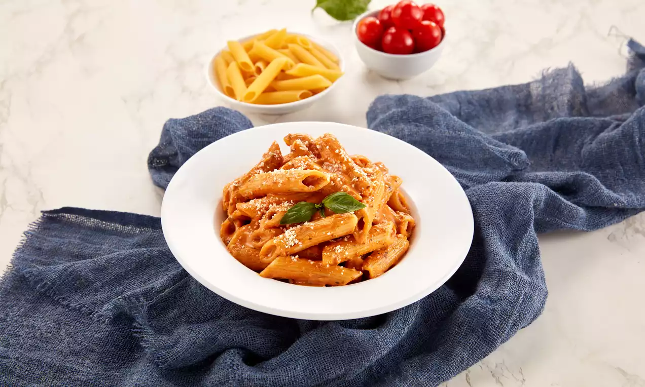 Penne coated in creamy orange vodka sauce topped with grated cheese and fresh basil served in a white bowl on a blue cloth