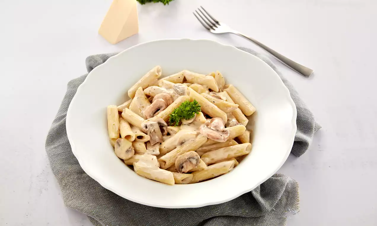 Penne pasta coated in a creamy mushroom sauce with brown mushroom slices, garnished with a green parsley sprig in a white bowl